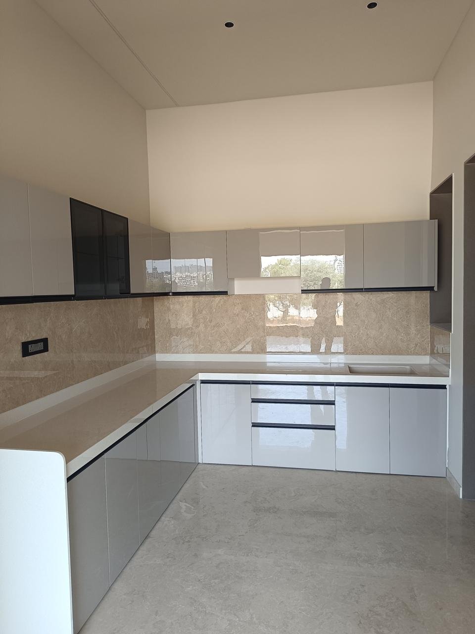 L-shaped modular kitchen in gloss grey with a beige stone backsplash