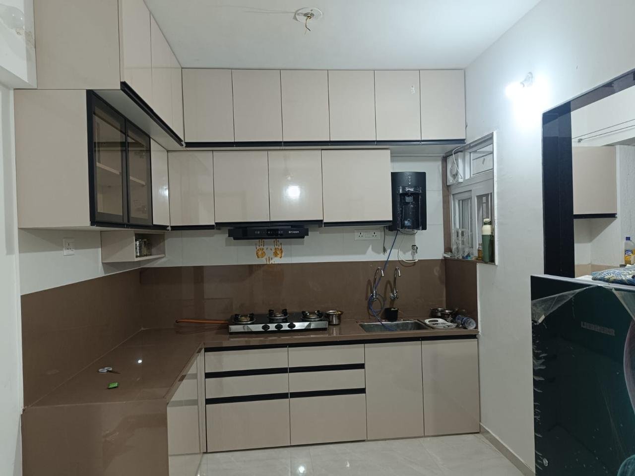 L-shaped modular kitchen in beige with a brown backsplash and dark glass cabinets