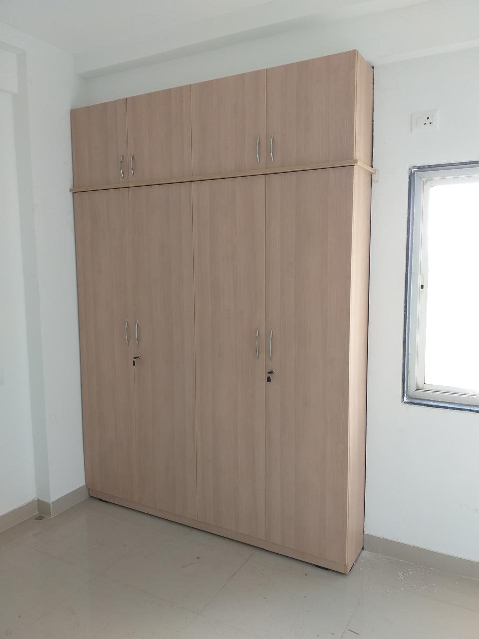Tall light-wood wardrobe with matching loft cabinets in an empty room
