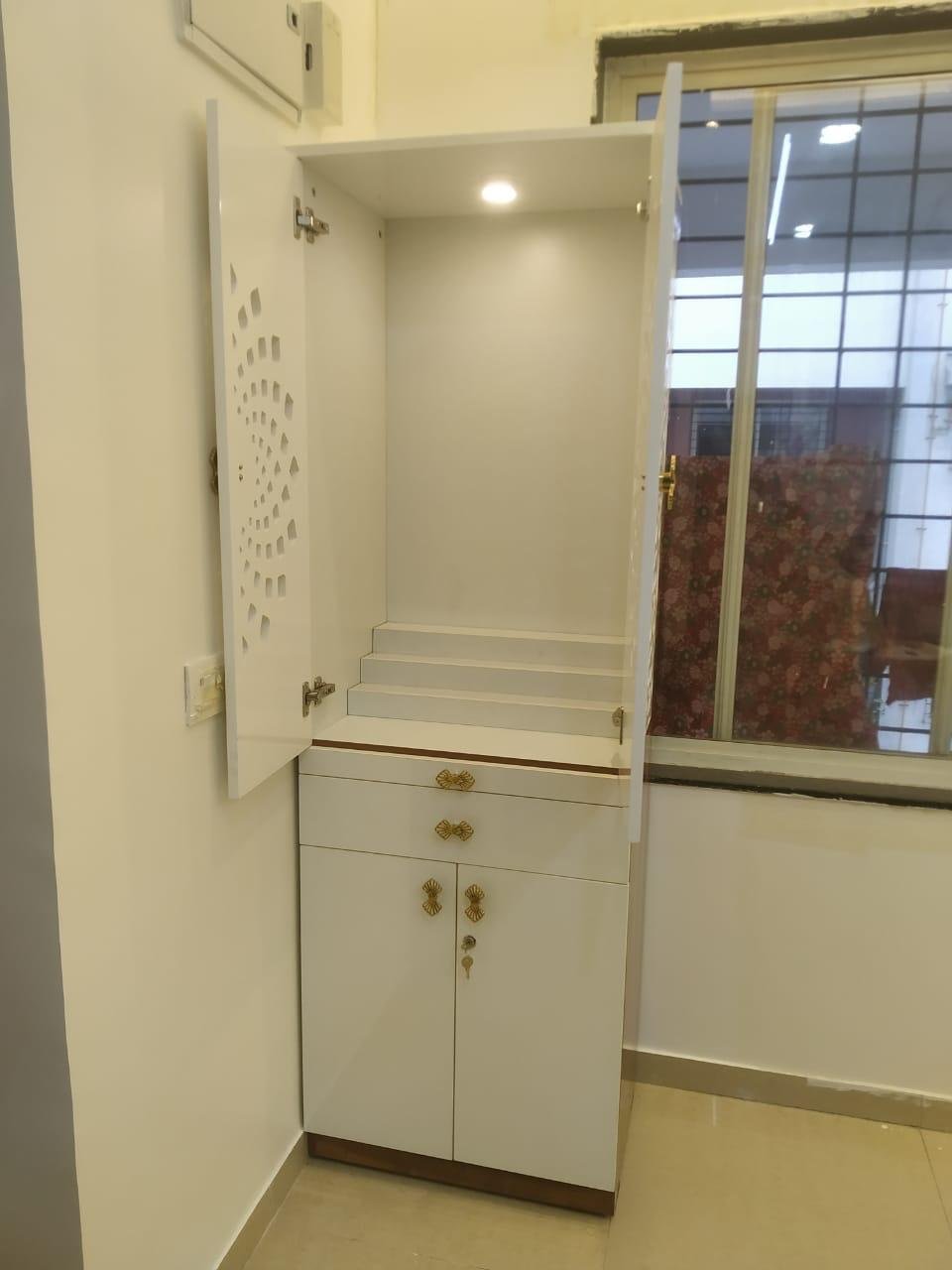 White mandir unit with jaali cut-out doors, a stepped altar and soft overhead lighting
